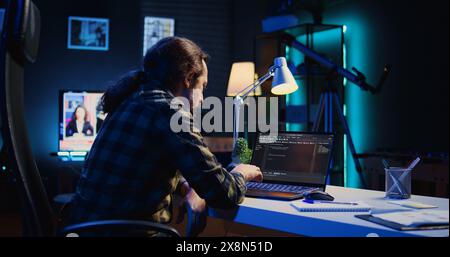 Experienced programmer writes code on laptop screen while in apartment office using Java programming languages. Developer remotely working on fixing database errors while working from home, camera B Stock Photo