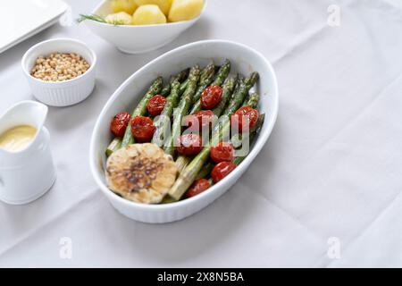 Representing a source of great dietary fiber, green asparagus baked in white baking dish, served with sauce hollandaise and boiled potatoes Stock Photo