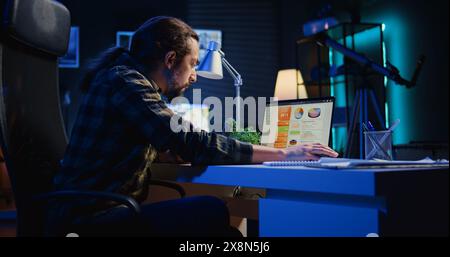 Man concerned about statistical data financial graphs on laptop screen while researching data for company project. Freelancer unhappy about business graphic figures, feeling stressed, camera B Stock Photo