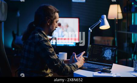 Programmer in living room office typing on keyboard, updating artificial intelligence neural networks, writing binary code scripts. Freelancing system administrator upgrading high tech AI Stock Photo