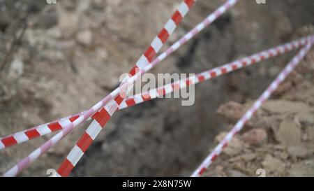 Red white barrier tape trenches. Focus on red and white barrier tape at construction site. Ribbons indicate dug trenches. Stock Photo