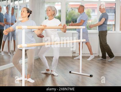 Elderly active women perform various ballet positions at the barre, men ...