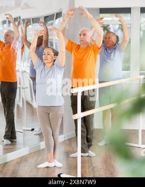 Active mature woman practicing fifth position holding by ballet barre together with others Stock Photo