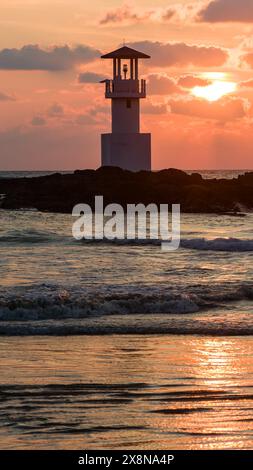 Tropical sunset behind a lighthouse on a small rock in the ocean Stock Photo