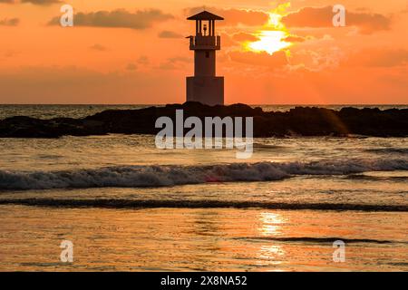 Tropical sunset behind a lighthouse on a small rock in the ocean Stock Photo