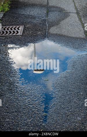 Water puddle on textured asphalt. Reflection of streetlamp, sky, clouds. Artistic illusion of blending elements. Stock Photo