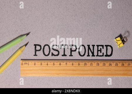 The word POSTPONED is written in a white notepad near a white cup of coffee on a light background. Stock Photo