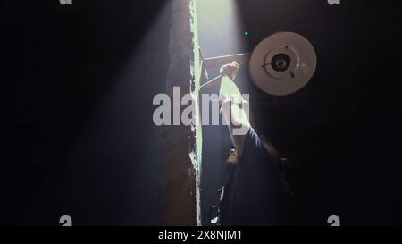 Low angle view of a male worker fixing vintage lantern on a dark background. Media. Man fixing ancient wooden street light. Stock Photo