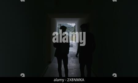 Two male silhouettes walking in dark long hotel corridor. Stock clip. Male figures in black hall. Stock Photo