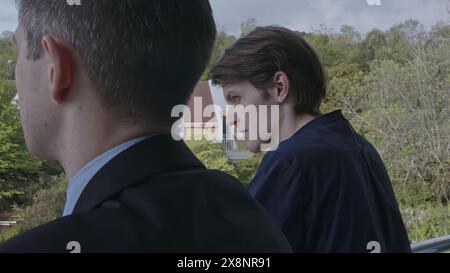Two young men standing on balcony and communicating. Stock clip. Business partners discussion and green spring vegetating on the background. Stock Photo