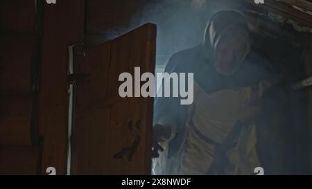 Elders in vintage robes coming inside wooden izba. Media. Men open the wooden beam door and coming inside old house. Stock Photo