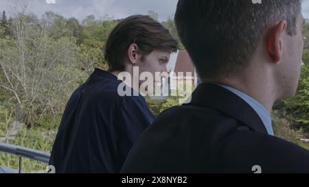 Two young men standing on balcony and communicating. Stock clip. Business partners discussion and green spring vegetating on the background. Stock Photo