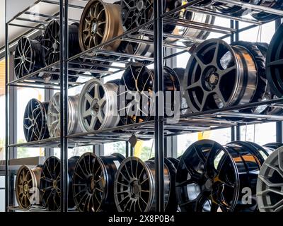 Scene of modern tyre store decoration with various designs of steel alloy wheels rim on metal shelf inside the building near huge glass window. Alloy Stock Photo