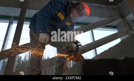 Man works as grinder at construction site. Clip. Man cuts metal pipe with sparks with circular saw. Sparks from cutting with circular saw on metal Stock Photo