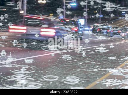 double exposure of night traffic in city and raindrops with bubbles in a puddle on wet road. Stock Photo