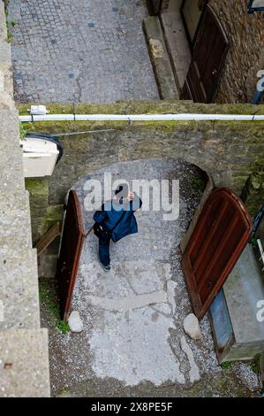 Person walking through an open archway in Carcassonne, captured from above, highlighting the medieval stonework and cobblestone paths. Stock Photo