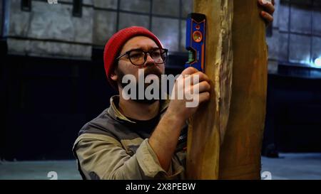Carpenter using spirit level on wooden vertical beam. Media. Bubble level tool in hands of a young male carpenter. Stock Photo