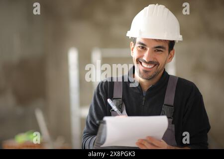 Happy construction worker holding clipboard looking at you in a house Stock Photo