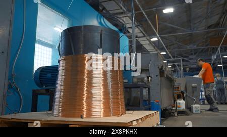 Worker starts machine with copper wire. Creative. Industrial cylinder with winding copper wire. Worker controls industrial machines with wires Stock Photo