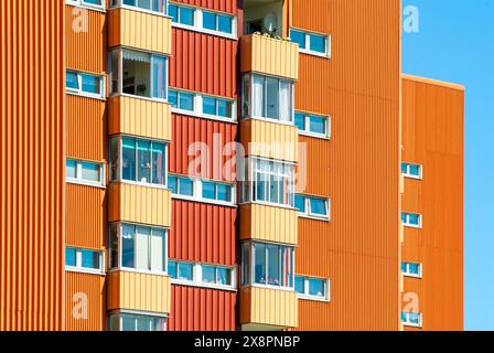 A tall building in shades of orange and red stands prominently, filled with numerous windows that catch the light. The architecture is modern and stri Stock Photo