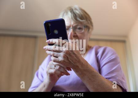 Mature woman in eyeglasses using mobile phone while sitting on a couch at home Stock Photo