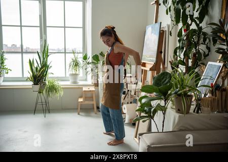Woman painter tying apron getting ready for creative work. Female artist at art workshop Stock Photo