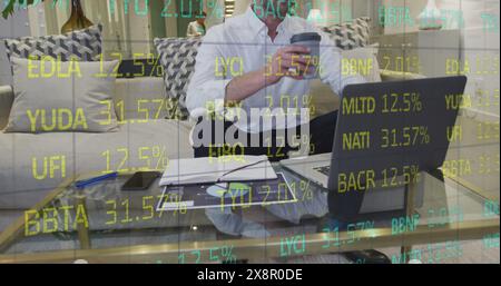 Image of trading board, caucasian man drinking coffee and writing in notepad while using laptop Stock Photo
