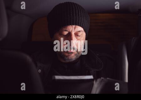 Serious man reading manual instruction book while sitting at the back seat of the car at night, selective focus Stock Photo