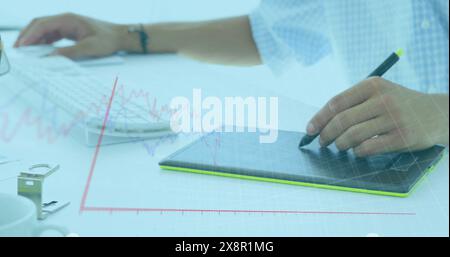 Image of graphs moving over caucasian businessman drawing on graphics tablet and using computer Stock Photo