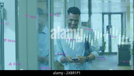 Image of multiple graphs and numbers moving over smiling biracial businessman using mobile phone Stock Photo