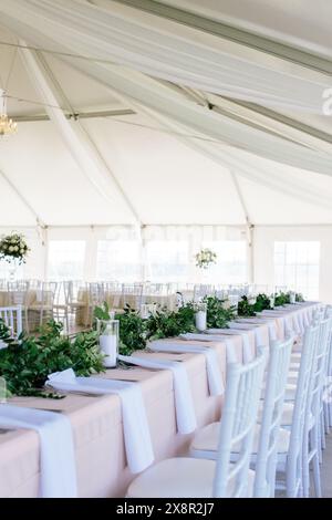 Elegant white wedding reception tent with long tables and greenery Stock Photo