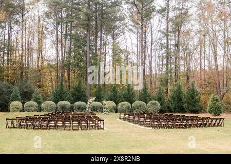 Outdoor wedding ceremony with rows of wooden chairs by trees Stock Photo