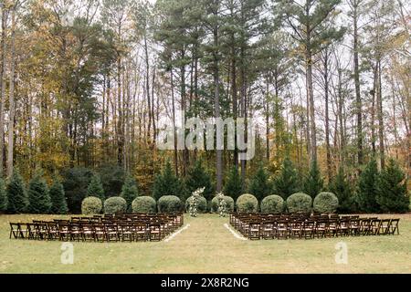 Fall wedding ceremony setup with rows of dark wooden chairs on grass Stock Photo