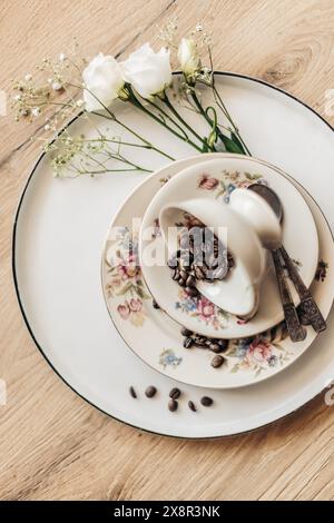Floral plates, white roses, and coffee beans on a wooden table Stock Photo