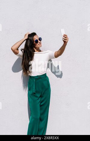 Female, trendy outfit posing for selfie, standing against background Stock Photo