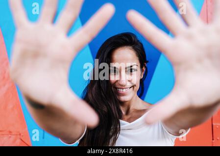 Smiling woman leaning against a wall while framing the face with hands Stock Photo