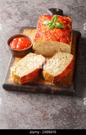 Tasty homemade ground baked chicken meatloaf glazed with ketchup closeup on the wooden board on the table. Vertical Stock Photo