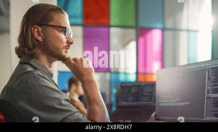 Male Senior Software Engineer Coding on Desktop PC With Multiple Monitors Setup and Laptop Aside in Stylish Office. Caucasian Man Developing Innovative SaaS Platform For Technological Startup Company. Stock Photo