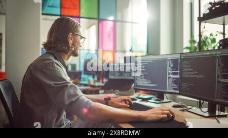 Professional Male Programmer Writing Code on Desktop Computer With Multiple Displays in Stylish Office. Caucasian Man Does Data Scraping For Artificial Intelligence Innovative Start-Up. Stock Photo