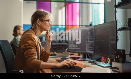Female Software Engineer Writing Code on Desktop Computer with Multiple Screens Setup in Coworking Office Space. Professional Caucasian Woman Working on SaaS Platform For Innovative Startup. Stock Photo