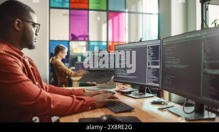 African American Man Writing Code on Desktop Computer With Multiple Monitors Set Up and a Laptop in Creative Office. Professional Data Scientist Using Software to Analyze Information From Internet. Stock Photo