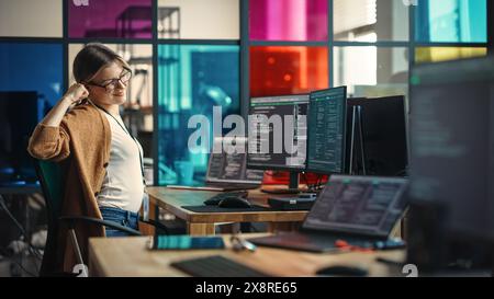 Young Caucasian Woman Programming On Desktop Computer With Two Monitors Setup in Spacious Office. Female Software Developer Creating SaaS Platform, Stretching Before Continuing to Work. Stock Photo