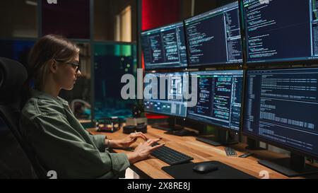 Female Cyber Security Specialist Writing Code On Deskop Computer with Six Displays in Dark Office. Caucasian Woman Controlls Digital Protection System, Monitoring Data, Debugging Software Errors. Stock Photo