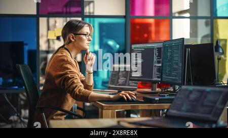 Female Junior Software Engineer Writes Code on Desktop Computer With Two Monitors and Laptop Aside In Stylish Office. Caucasian Woman Working On Artificial Intelligence Service For Big Tech Company. Stock Photo