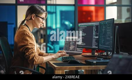 Young Caucasian Woman Programming On Desktop Computer With Two Monitors Setup in Spacious Office. Female Software Developer Creating SaaS Platform For Businesses in Innovative Start-up Company. Stock Photo