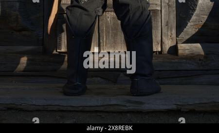 A medieval warrior legs in ancient shoes against wooden house doorstep. Media. Strong ancient warrior. Stock Photo