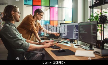 Male Programmer Shows Progress to Female Start-Up CEO on Desktop Computer in Creative Office Space. Caucasian Man and Woman Discussing New Features For Artificial Inteligence Software. Stock Photo