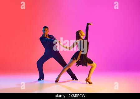 Portrait of young talented couple practicing ballroom dancing in motion in neon lighting against vibrant gradient background. Stock Photo