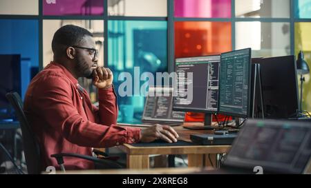 Male Senior Software Developer Writing Code On Desktop Computer With Two Displays Setup in Stylish Office. Black Man Working On Mobile Application For Online Service of Modern Start-up Company. Stock Photo