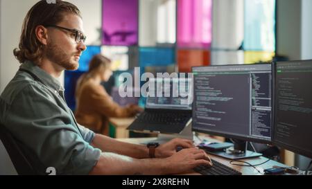 Caucasian Male Software Engineer Coding on Desktop Computer With Multiple Displays in Creative Office. Young Handsome Man Writing Code For Mobile Application In Tech Start-Up Company. Stock Photo